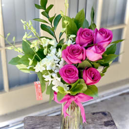 Pink roses and white orchids in a glass vase with a pink ribbon