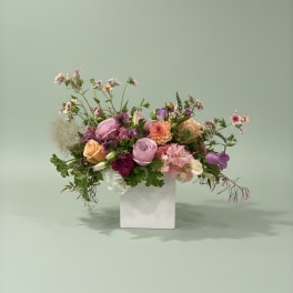 Mixed pink, peach, and purple flowers in a white vase