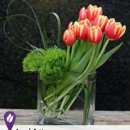 Pink and yellow tulips in a clear glass vase with green decorative accents