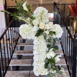 White floral cross arrangement on an easel with roses and calla lilies