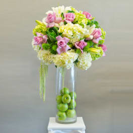 Pink roses and white hydrangeas in a tall glass vase with green apples
