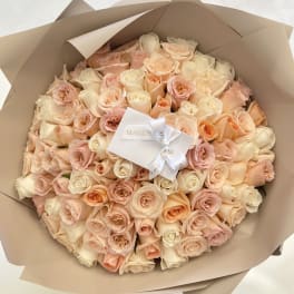 Bouquet of blush and cream roses wrapped in tan paper with a white ribbon