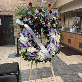 Large funeral wreath of red roses and white flowers on an easel with patriotic ribbons