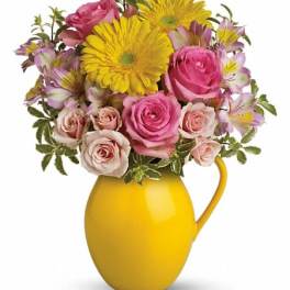 Pink roses and yellow daisies arranged in a yellow pitcher vase