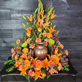 Orange lilies and roses arranged around a bronze urn centerpiece