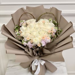 Heart-shaped bouquet of white and blush roses wrapped in taupe paper