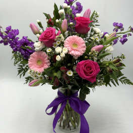 Mixed bouquet of pink and purple flowers in a glass vase with a purple ribbon