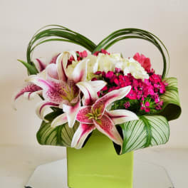 Pink lilies and mixed blooms in a lime green vase with arched greenery