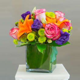 Colorful bouquet of roses, lilies, and mums in a square glass vase