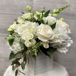 White roses and hydrangeas arranged in a square box with greenery