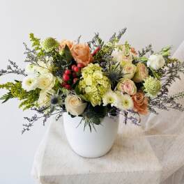 Mixed bouquet of peach, white, and green flowers in a white vase