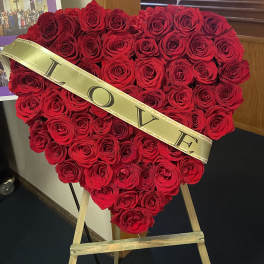 Heart-shaped red rose arrangement on an easel with a gold LOVE sash