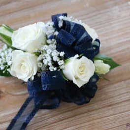 White rose corsage with navy ribbon on a wooden surface