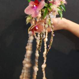 Handheld floral piece with pink orchids and hanging shells