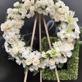 White floral wreath on a wooden easel with roses and lilies