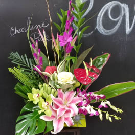 Tropical floral arrangement with pink lilies, orchids, and red anthuriums