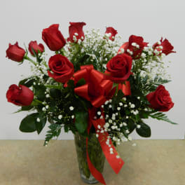 Red roses in a clear glass vase with white baby's breath and a red ribbon