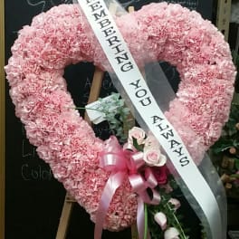 Pink heart-shaped floral wreath with a memorial ribbon on an easel