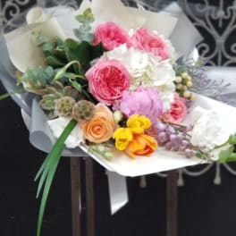 Mixed bouquet of pink, white, yellow, and peach flowers wrapped in paper