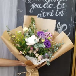 Hand-tied bouquet of purple, white, and pink flowers in brown paper