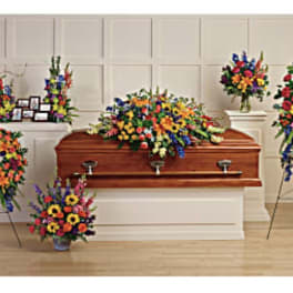 Colorful funeral casket spray with standing floral tributes around a wooden casket