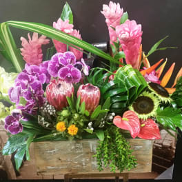 Tropical floral arrangement with orchids, protea, and bird of paradise in a wooden box