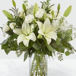 White lilies and roses arranged in a clear glass vase