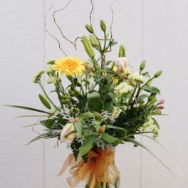 Tall mixed flower arrangement in a glass vase with a candle beside it
