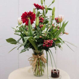 Tall bouquet of red and white flowers in a glass vase with a ribbon bow