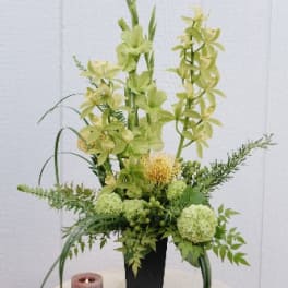 Tall green floral arrangement in a black vase with a pink candle beside it