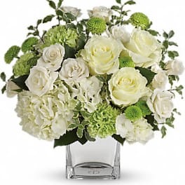 Short white and green flower arrangement with roses and hydrangeas in a clear glass cube vase