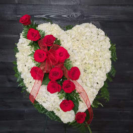Heart-shaped white floral arrangement with red roses and a red ribbon