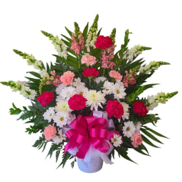 Pink and white flowers arranged in a white vase with a magenta bow