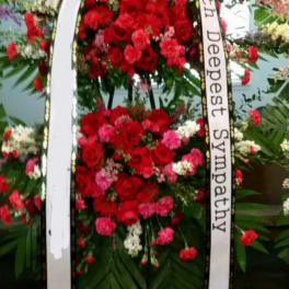 Standing sympathy wreath of red and pink flowers with white ribbon