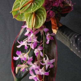 Handheld bouquet with purple roses, orchids, and large tropical leaves