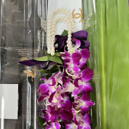 Purple orchid lei with pearl beads and ribbon in clear packaging