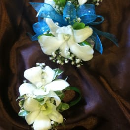 White orchid corsages with blue ribbon on dark fabric