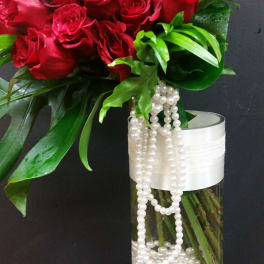 Red roses in a tall glass vase with white bead strands