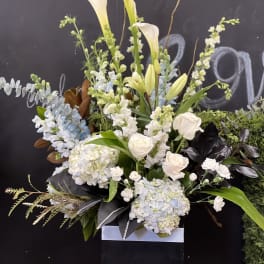 Tall white floral arrangement with lilies, roses, and hydrangeas in a black box