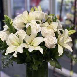 White lilies and roses arranged in a clear glass vase