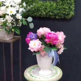 Pink and purple flowers arranged in a white vase on a stool