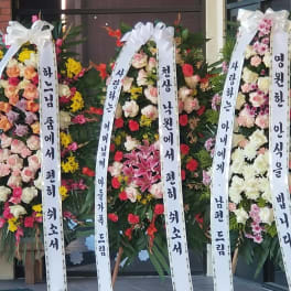 Three tall floral standing wreaths with white ribbon banners and mixed blooms