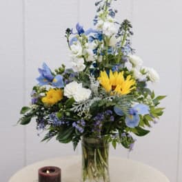 Blue and white floral arrangement in a glass vase with a candle beside it