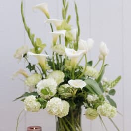 White calla lilies and round white blooms in a glass vase