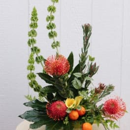 Tropical floral arrangement with red pincushion blooms and yellow calla lilies