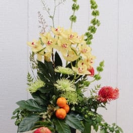 Tall floral arrangement with yellow orchids and red blooms in a container