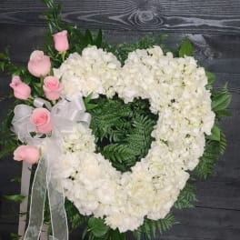 Heart-shaped white floral wreath with pink roses and a white ribbon bow