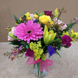 Colorful mixed bouquet in a clear glass vase with a pink ribbon