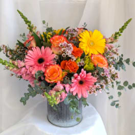 Bright arrangement of pink gerbera daisies, orange roses, and yellow blooms in a ribbed metal vase