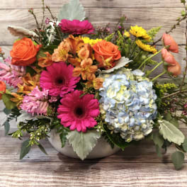 Mixed bouquet with roses, gerbera daisies, hydrangea, and orange blooms in a low vase